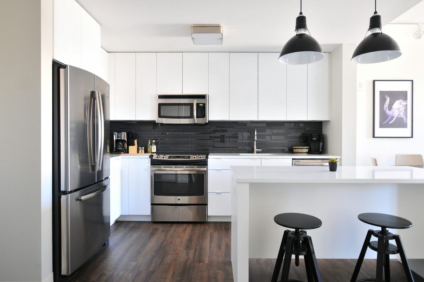 Modern condo kitchen with stainless steel appliances, white cabinets, and pendant lights