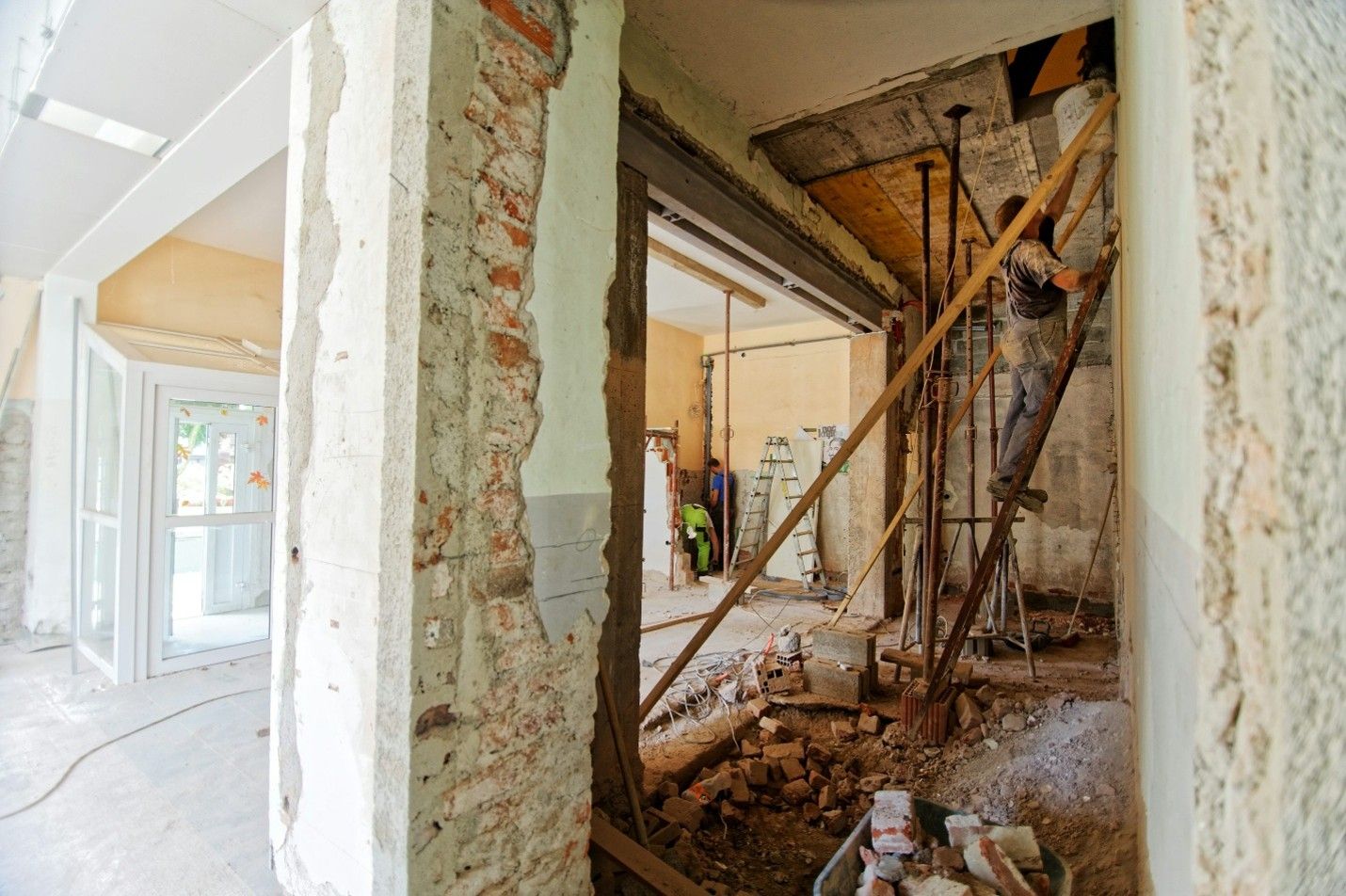 Interior renovation in progress with exposed brick, support posts, and a worker on a ladder
