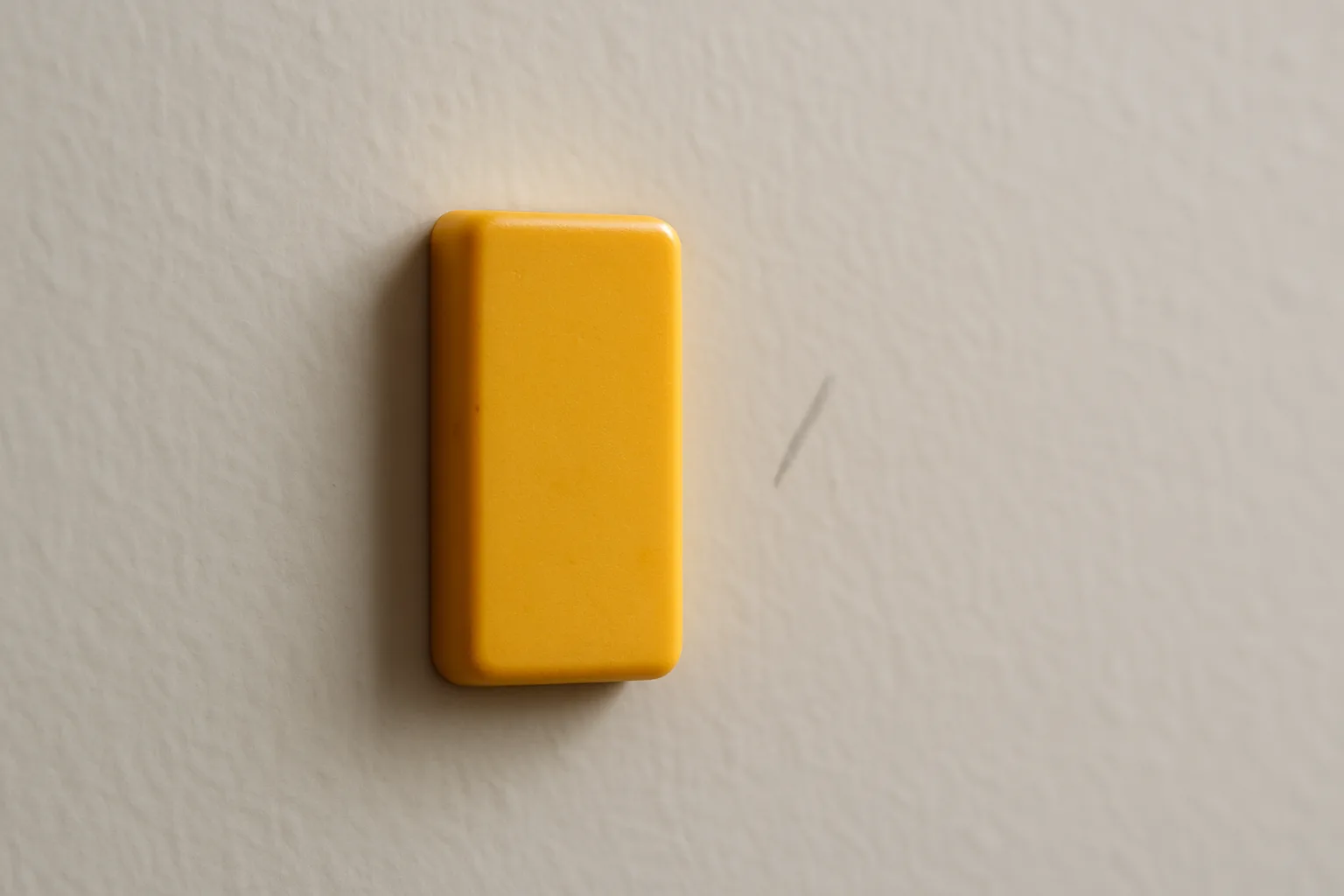 A small unbranded magnetic stud finder stuck to a painted drywall wall next to a light pencil mark