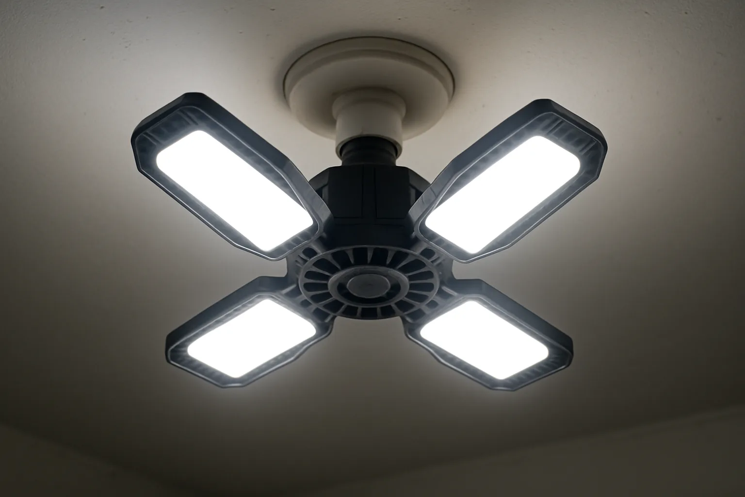 Four-panel deformable LED garage light with its panels folded outward, screwed into a ceiling light socket and glowing bright white