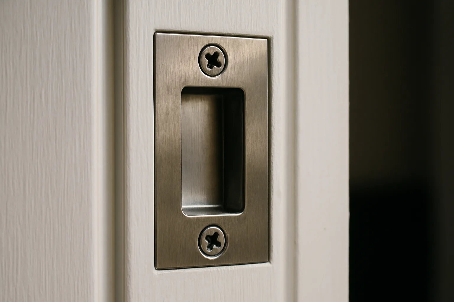 Close-up of a brushed-steel strike plate set into a white painted door frame