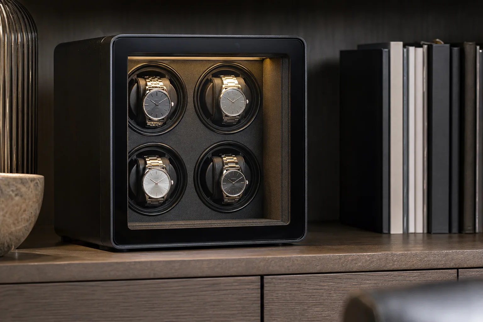 Four-watch winder cabinet with a lit interior and glass door on a home office shelf with four steel automatic watches on rotating cushions