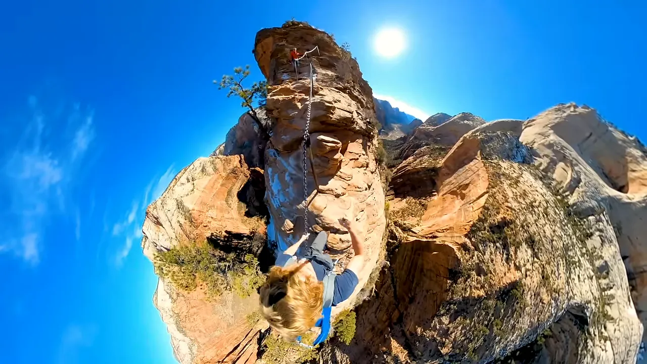 Hikers ascending a narrow, steep trail with chains on a sandstone ridge
