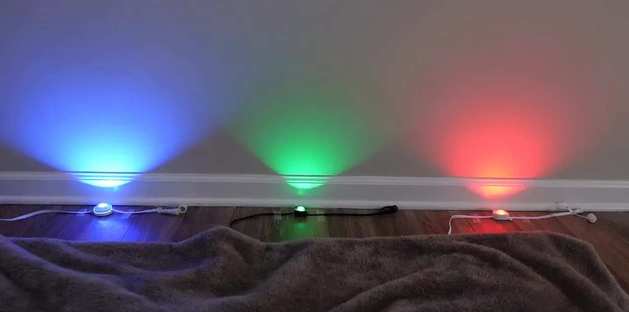 Three puck lights showing Christmas-sequence colors on a wall, illustrating cone shapes and color blending