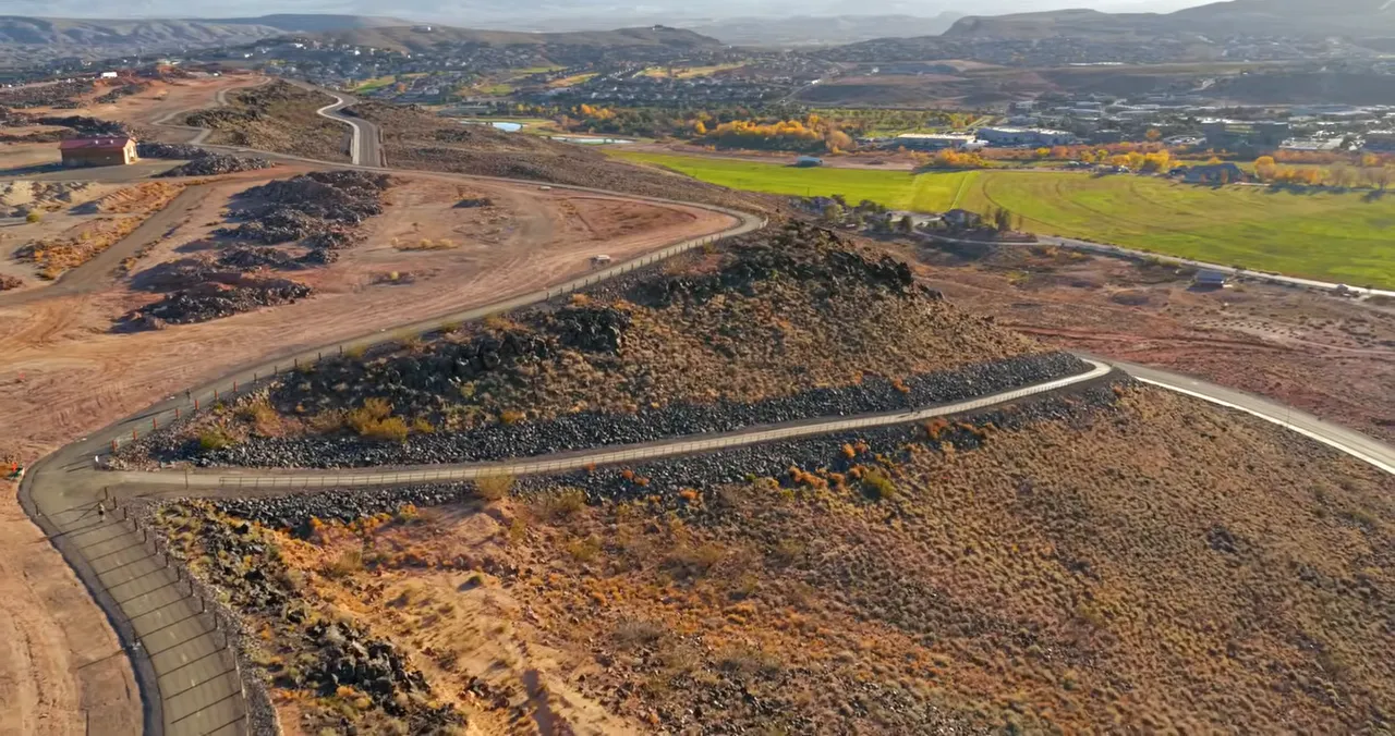 Paved rim trail winding around a rocky knoll on the St. George bluff with fields and town visible in the distance.