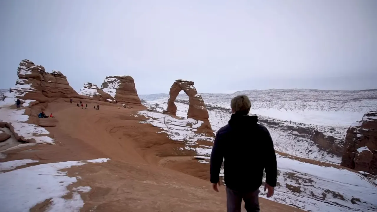 Visitor standing in front of Delicate Arch framing with red rock formations